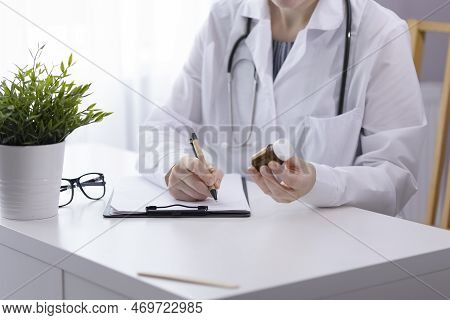 A Doctor With A Stethoscope Around His Neck, In A White Coat, Sits At A White Stoma, Looks At A Glas