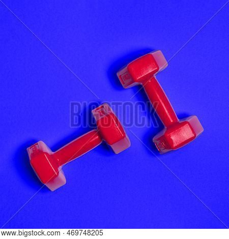 Two Bright Red Dumbbells Are Isolated On Blue Background. Sport And Health Concept