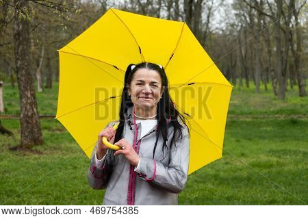 Happy Senior Woman In Yellow Rain Coat With Yellow Umbrella Encouraging Self-care And Relaxation, Us