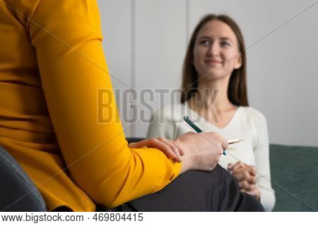 Focus On The Psychologist's Hand With A Pen. Smiling Young Woman Listens To A Psychologist At The Re