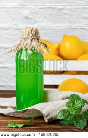 Lemon Syrup In Glass Bottle And Fruits In The Crate On The Background. Side View Of Fresh Citrus.
