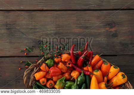 Wicker Basket With Many Different Fresh Chilli Peppers On Wooden Table, Top View. Space For Text