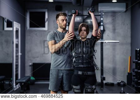 Female And Male Confident Athletes Train Indoors At The Gym. Woman Is Dressed In Ems Technology In A