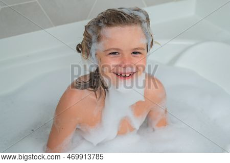 Child Boy Washing With A Bubbles In Bath. Cute Child Bathes, Lying In A White Bath With Foam From So