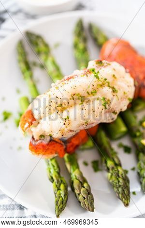 Sering Garlic Lobster Tails With Steamed Asparagus And Lemon Wedges On A White Plate.