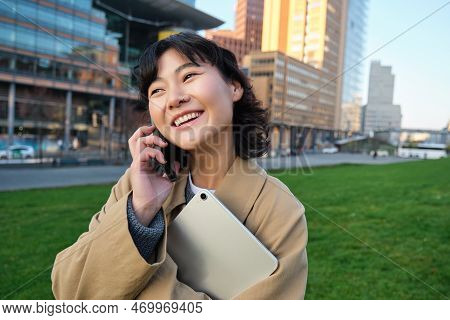 University Lifestyle. Young Asian Student, Girl With Tablet And Notebook, Talks On Mobile Phone Whil