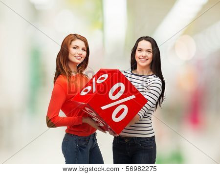 shopping, sale, mall and gift sconcept - two smiling teenage girls with percent sign on red box at shopping mall