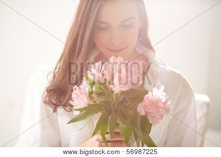 Portrait of lovely lady looking at bunch of flowers in her hands