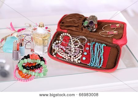 Handbag with accessorises and perfumes in bottles on table on  home interior background