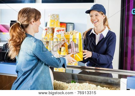 Happy female seller giving popcorn paperbag to pregnant woman at cinema concession stand