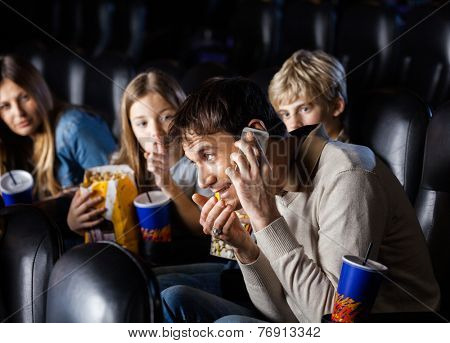 Angry family looking at man communicating on mobilephone in cinema theater