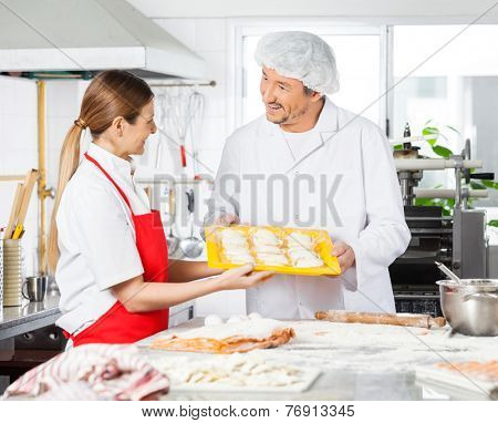 Happy male and female chefs discussing while holding pasta tray in commercial kitchen