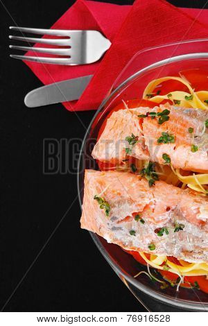 fresh fried natural pink salmon on italian traditional tagliatelle backed with tomato and vegetables served over black wooden table