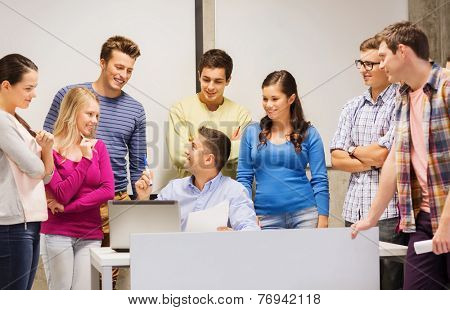 education, high school, technology and people concept - group of smiling students and teacher with papers, laptop computer in classroom