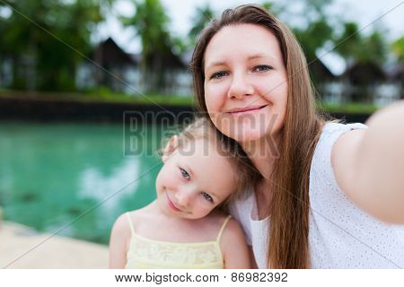 Happy family mother and her adorable little daughter on summer vacation taking selfie with smartphone