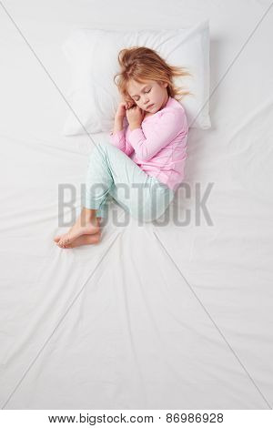 Top view of little girl sleeping in Foetus pose