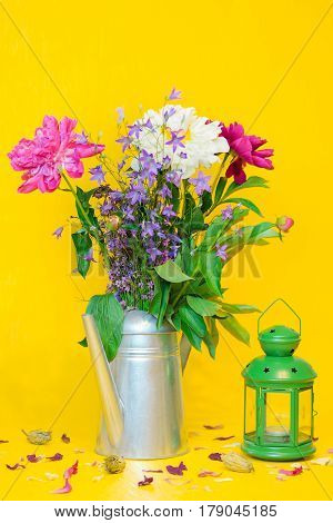 A still life with a beautiful white and purple peonies bouquet and a green lantern on the blurred yellow background