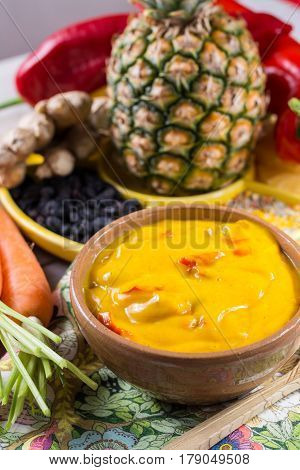 Bowl of vegetable curry sauce and ingredients that go into making it - paprika chili pepper carrot pineapple gember. Used widely in Indian food.