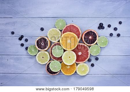 Variety of citrus fruits (orange blood oranges lemons grapefruits and limes) with blueberries over a blue rustic wood table top. Image shot from overhead.