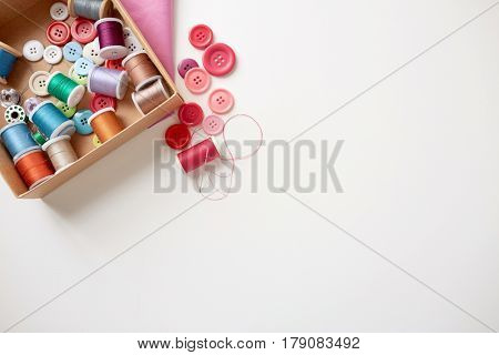needlework, craft, sewing and tailoring concept - box with thread spools and buttons on table