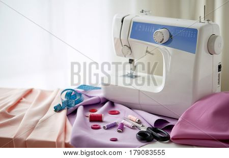 needlework, technology and tailoring concept - sewing machine with scissors, buttons, tape measure and fabric