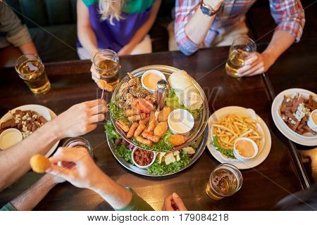 leisure, food, drinks, people and holidays concept - friends eating snack and drinking beer at bar or pub