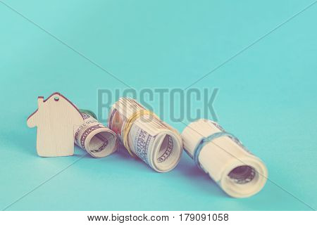The concept of financial savings to buy a house. Mini model house dollars in rolls isolated on the blue background. Toned.