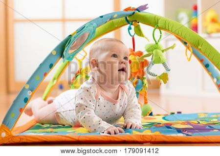 Happy seven months baby girl plays lying on colorful playmat in nursery