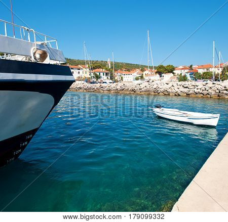 White boat in the transparent turquoise sea water near a ship with depth marks. Small village with many white houses and several masts. Blue cloudless sky. Dugi otok Croatia
