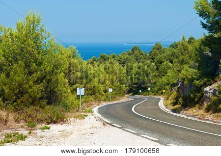 Empty road winding among rocks and lush green hills with pine trees against the azure blue sea on a warm summer day. Blue cloudless sky on the back. Dugi otok Croatia