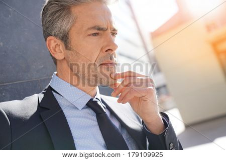 Portrait of businessman waiting outside building, leant on wall