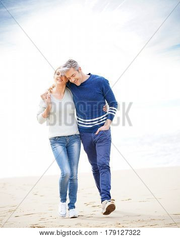 Middle-aged couple walking on the beach, full length