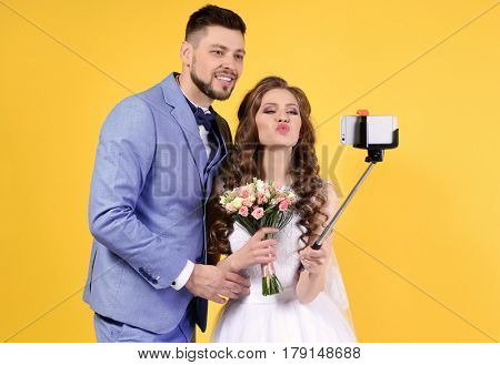 Happy wedding couple making selfie on color background