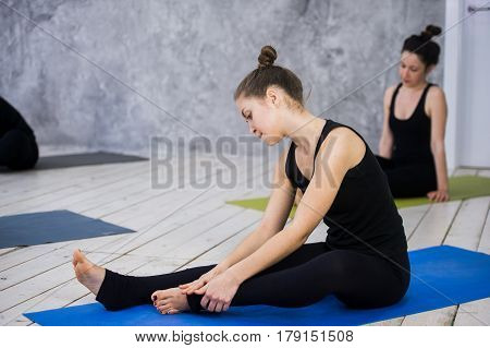 Shot of young women warming up before yoga session. Young people sitting on exercise mat in yoga class