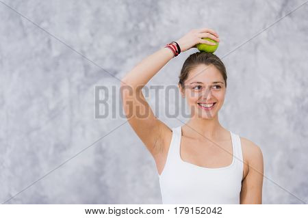 Smiling woman doing yoga pose holding apple on her head.