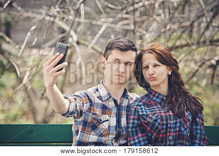 Young cheerful couple making selfie on a bench on a background of branches