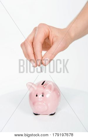 Cropped View Of Woman Putting Coin In Piggy Bank On White