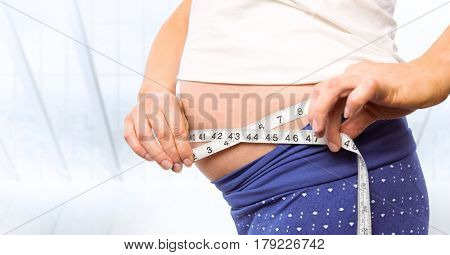 Digital composite of Pregnant woman mid section with measuring tape against blurry window