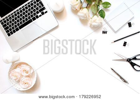 Minimalistic feminine workplace with laptop keyboard, pen, white candles, notebook, office clips and roses in flat lay style. White background, top view, frame