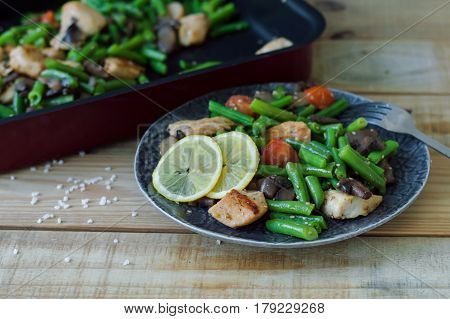 Portion of hot salad with green beans chicken meat mushrooms and cherry tomatoes served with lemon ans sesame seeds on wooden table