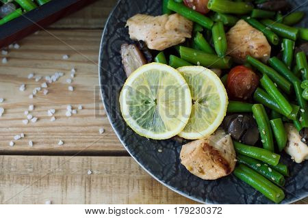Plate with baked green beans chicken breast mushrooms red cherry tomatoes sesame seeds and lemon. Hot salad. Balanced and healthy meal