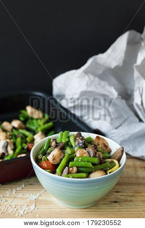 Vertical photo of hot salad in a blue bowl: green beans chicken meat cherry tomatoes lemon mushrooms and sesame seeds