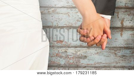 Digital composite of Wedding couple holding hands against wood