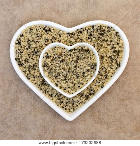 Hulled hemp seed super food in a heart shaped dish on natural hemp paper background.