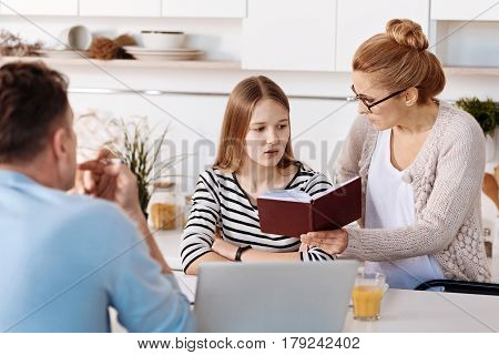 Bad grades. Caring strick mother checking results of studying of her daughter while sitting together in the kitchen