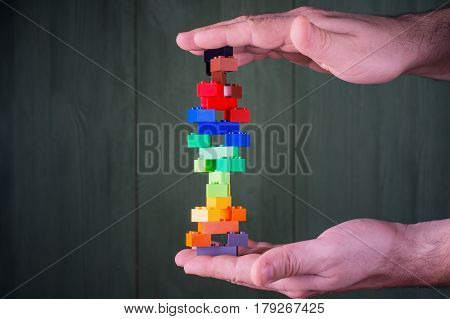 Human hand holding abstract construction from colorful plastic stack blocks. The concept of logical thinking.