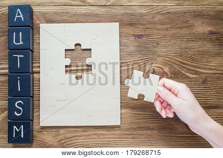 Black wooden cubes with word AUTISM on wooden background and hand with a piece of puzzle on a wooden background top view flat lay. Autism Spectrum Disorder (ASD). Autism awareness.