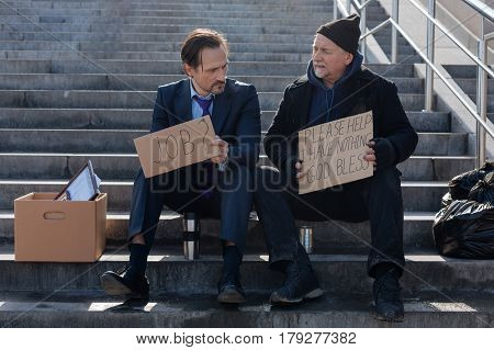 Everything will be great. Jobless young man wearing costume putting thermos near his leg while looking at poster of his new friend