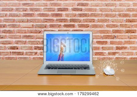 Connecting to the online service concept. Laptop and mouse on wooden table and brick wall with Telecommunication tower image on screen and online service icon