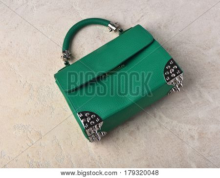 Nice beautiful small womans leather green fashionable bag with decorative metallic spikes or thorns on white textured background